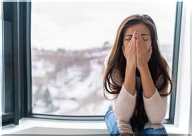 A woman sitting and crying by a window.