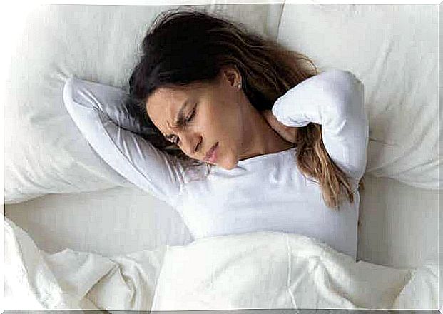 A woman lying in bed holding her neck in pain