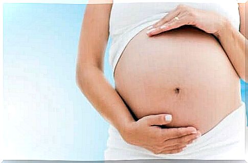 A pregnant woman in white, holding on to the abdomen, one of the contraindications to marjoram is use during pregnancy