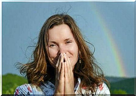 A woman praying in front of a rainbow.